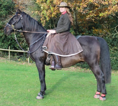 Customer wearing her Brown hand crafted, waxed cotton riding skirt on her black horse stood in a feild.