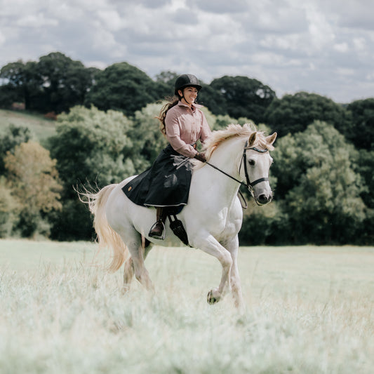 Woman wearing handcrafted riding habit riding across an open feild.