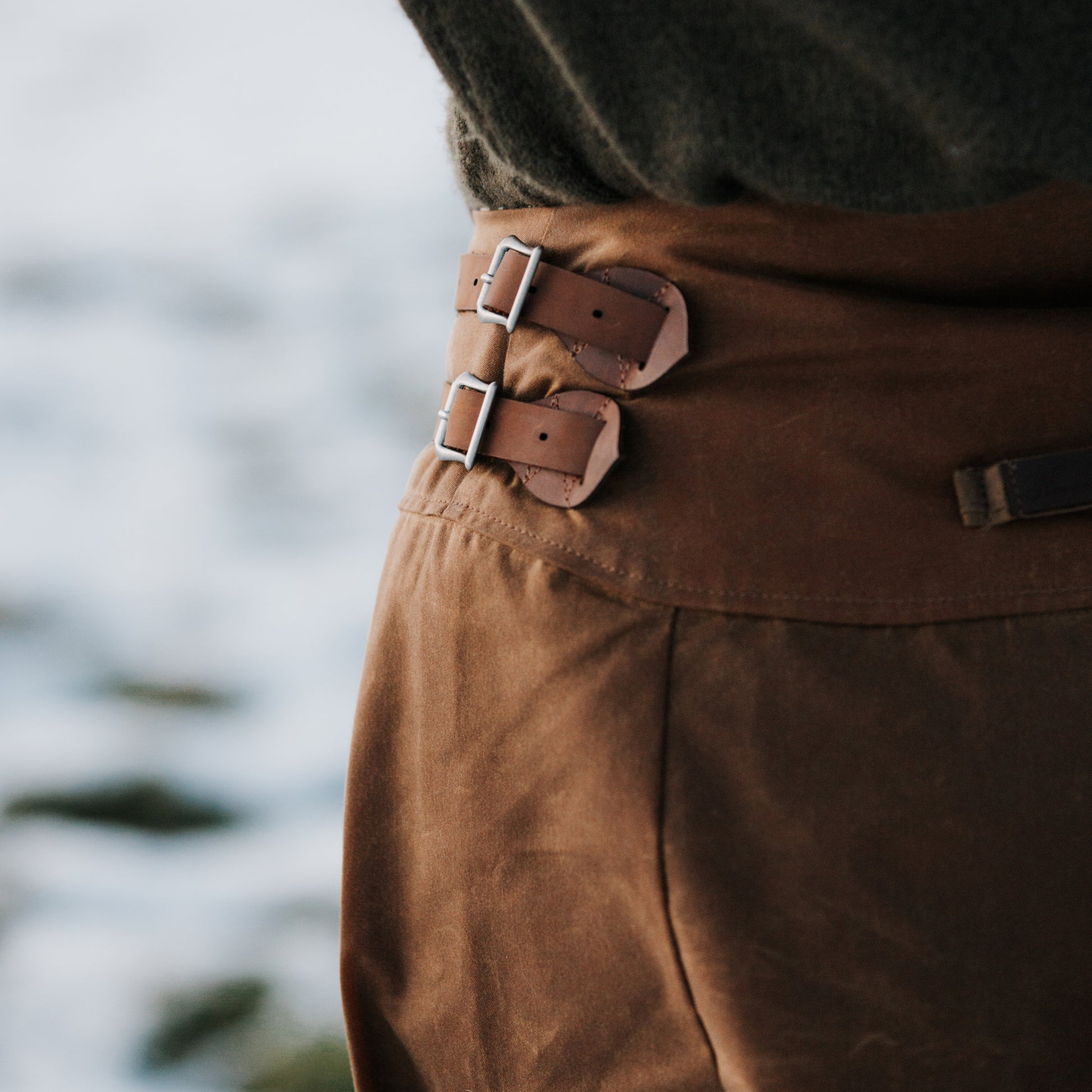 Close up of leather buckles on the side of a handcrafted waxed cotton habit.