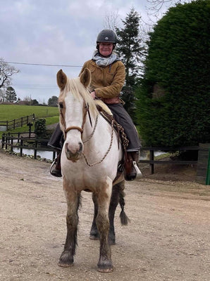 Customer wearing her bespoke riding skirt while sat on her skewbald horse with the countryside behind them.