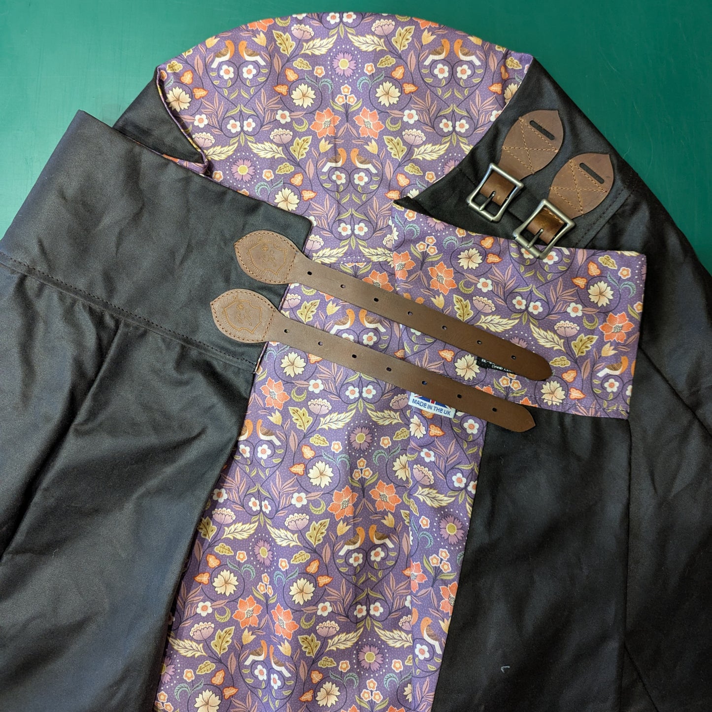 An areial view of the Isabella riding skirt folded to show off the Vinatge brown waxed cotton and the purple floral lining