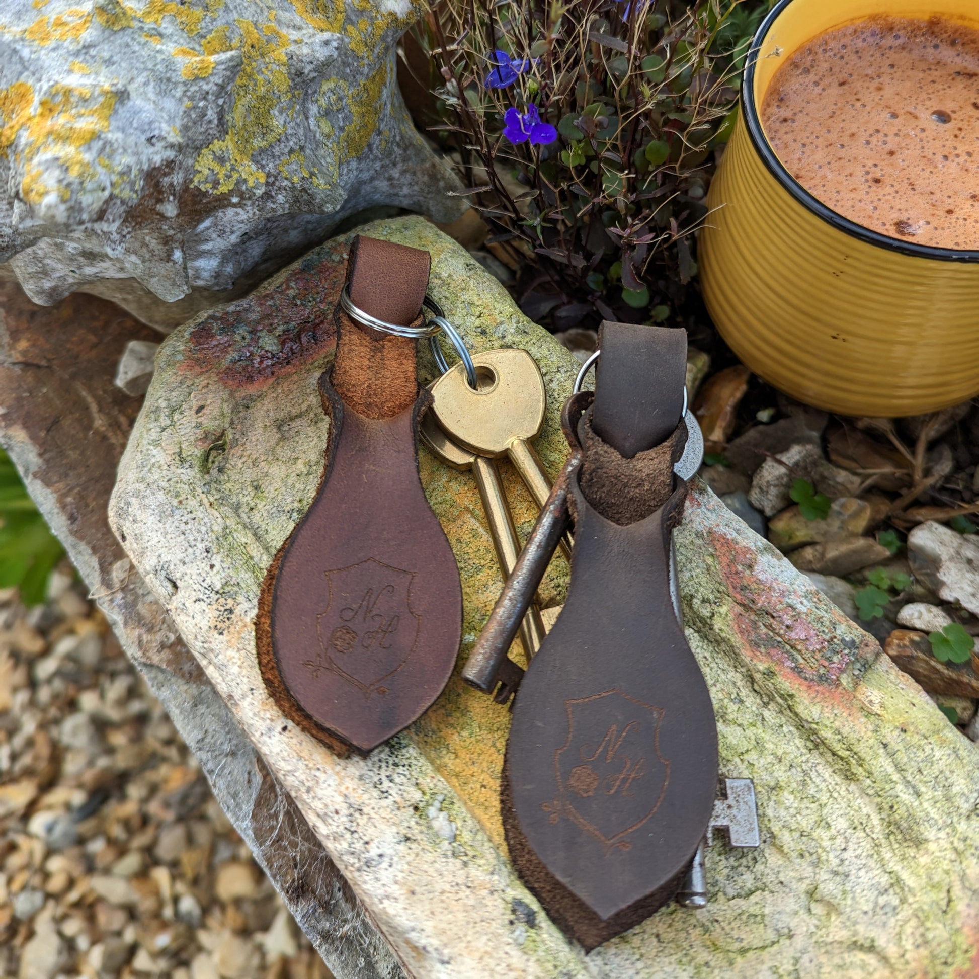 Two sets of leather key rings next to a mug of hot chocolate outside in a garden.