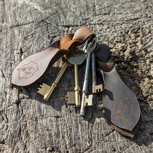 Leather keyrings resting on some wood with the sun shining down on them.
