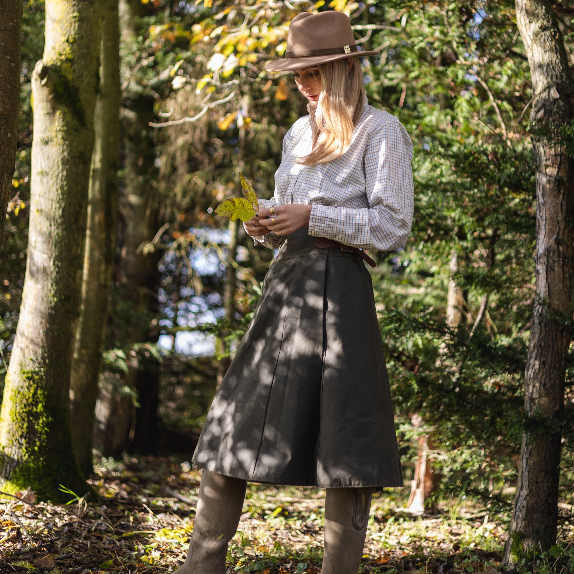 Handcrafted country clothing, worn in the woods with dappled light coming down on to the model while she looks at a autumn leaf.