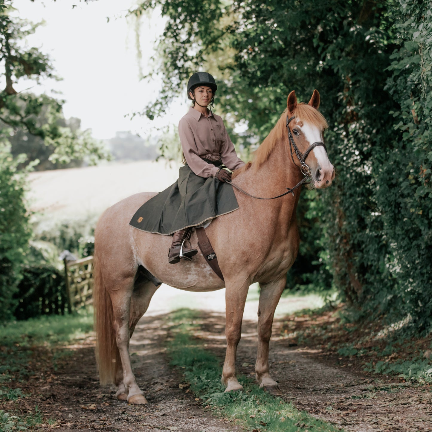British-made riding habit in green being worn on a roan coloured horse, stood relaxed in a country lane.