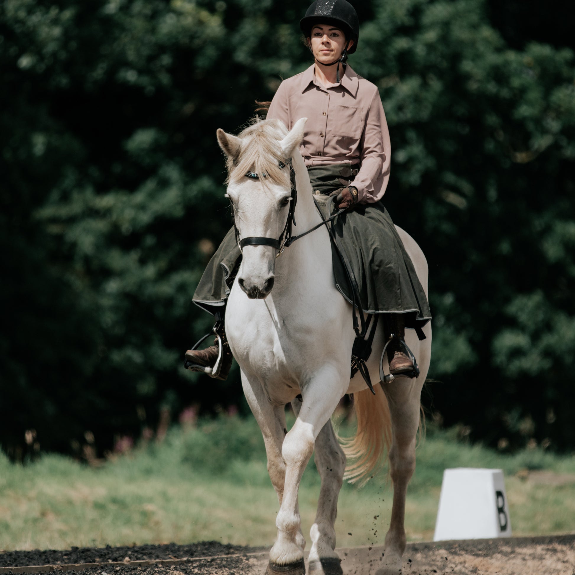 Woman wearing handcrafted riding habit while schooling a grey horse in her outdoor arena.