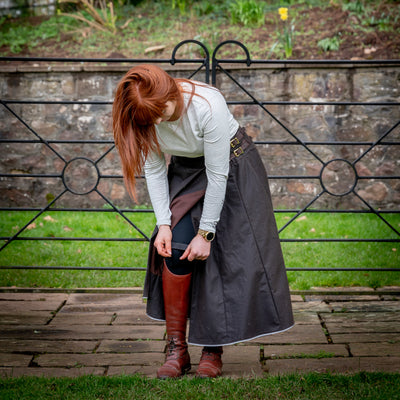 Hand crafted waterproof riding skirt having its leg straps adjusted stood in front of a metal gate.
