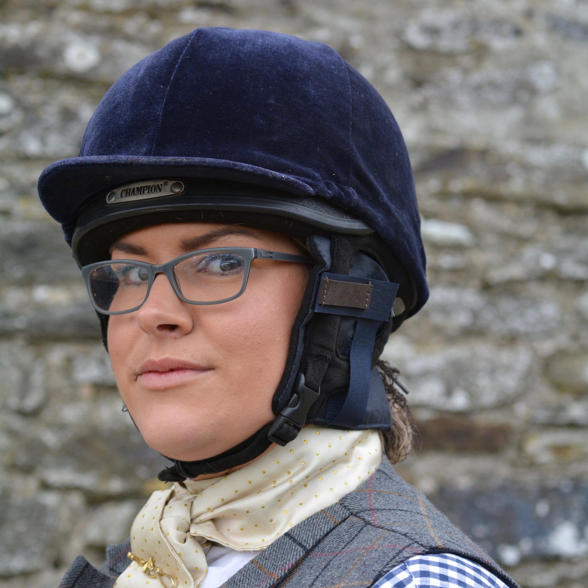 Handcrafted waxed ear warmer in a riding hat being worn by a young lady stood infront of a stone wall