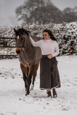 Customer leading her horse though the snow while wearing her Original Moorland waterproof habit.