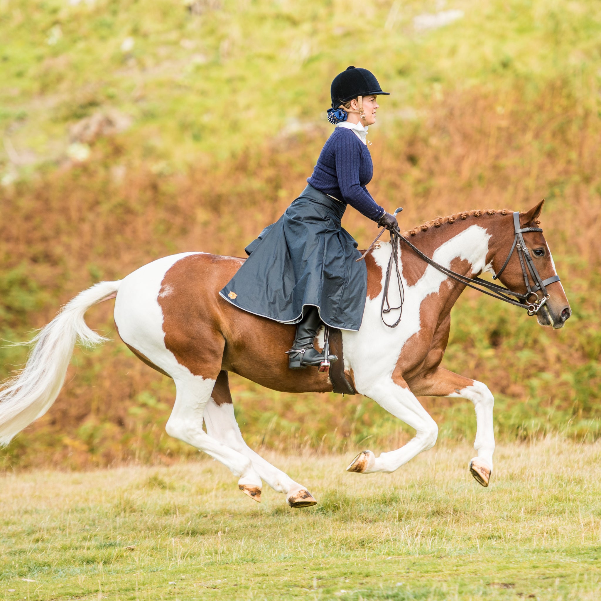 Sideview of galloping horse with rider wearing a navy waxed cotton riding skirt.