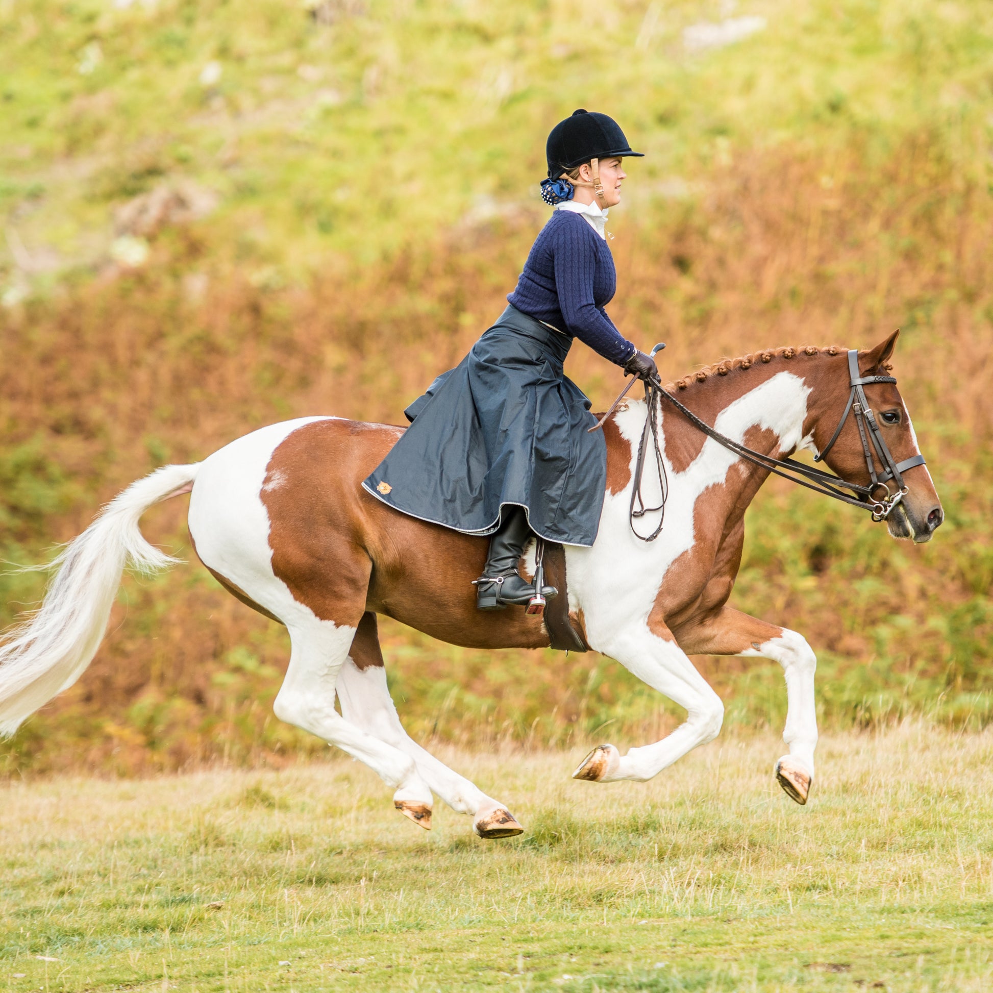 Sideview of galloping horse with rider wearing a navy waxed cotton riding skirt.
