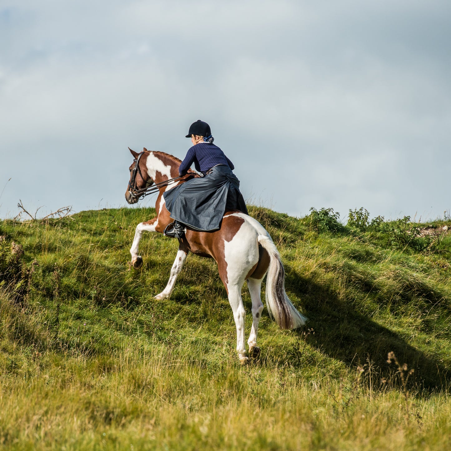 British made riding habit being worn while cantering up a steep slope while the rider is in a forward pose position.
