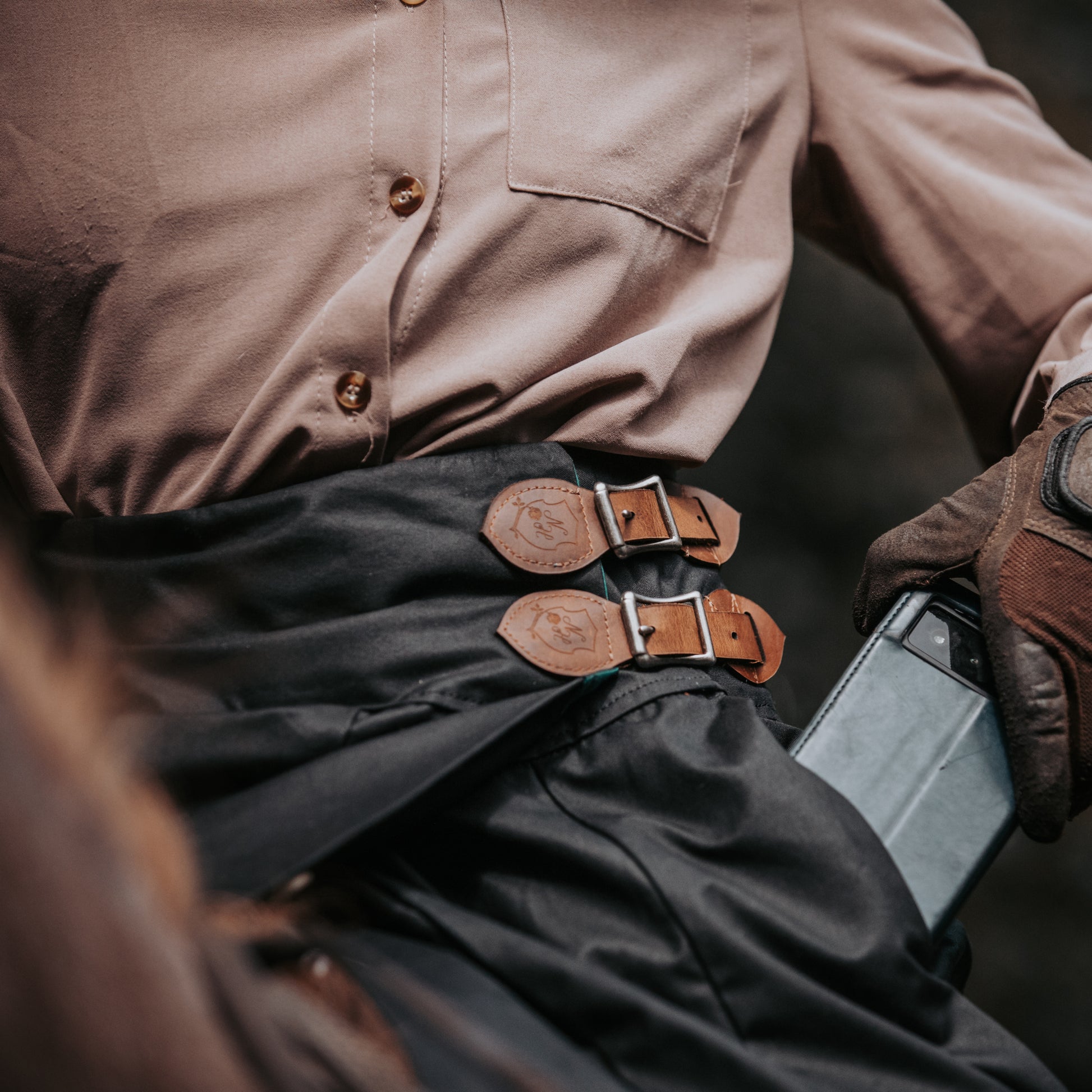 hand crafted waxed cotton riding habit in black being worn on horse showing a close up of a phone being put into its pocket.