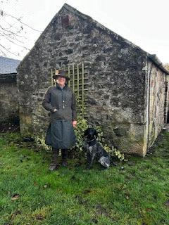 Customer stood in front of a stone barn wearing her Compass habit with her dog by her side.