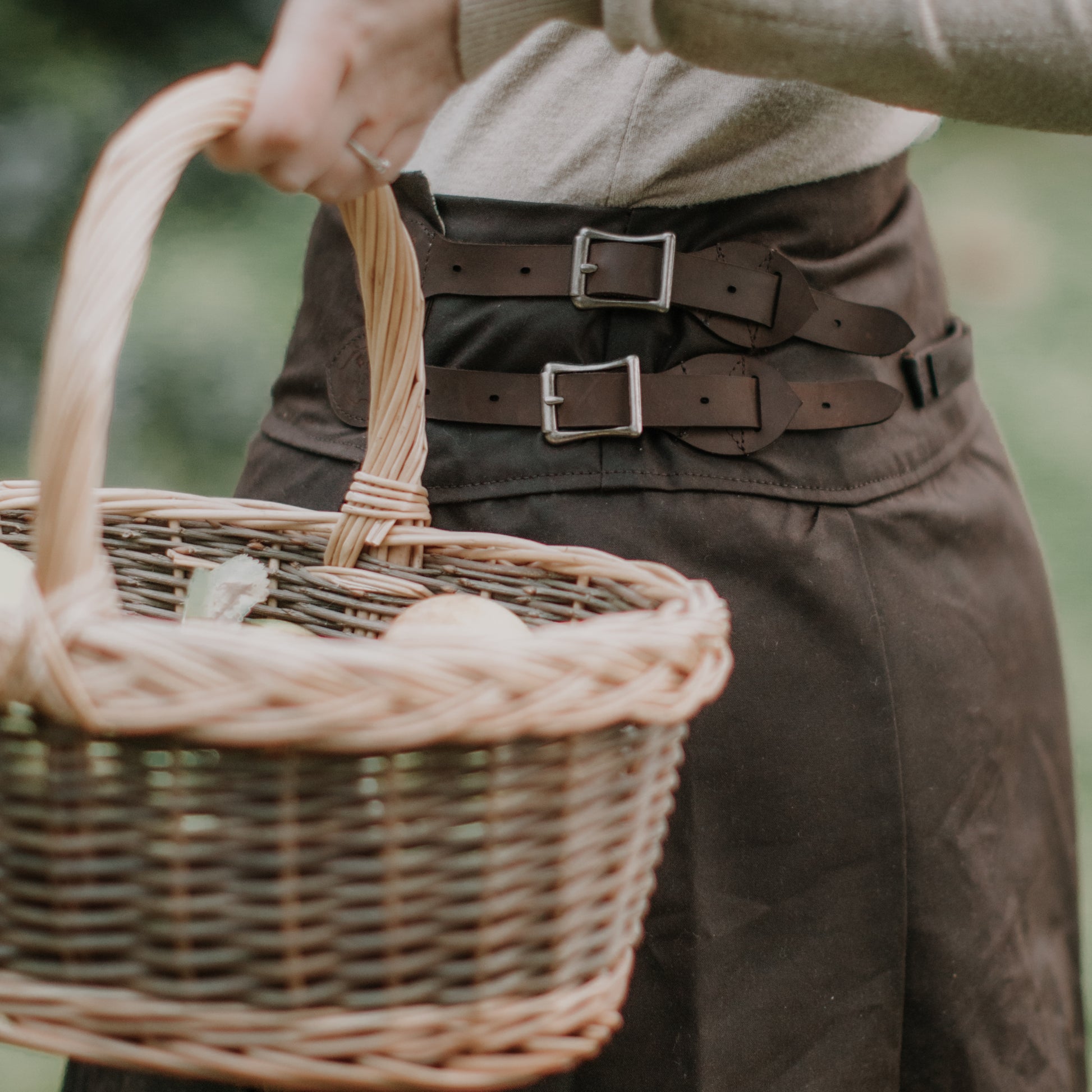 Apple picking basket being carried infront of a hand crafted brown waxed cotton habit.