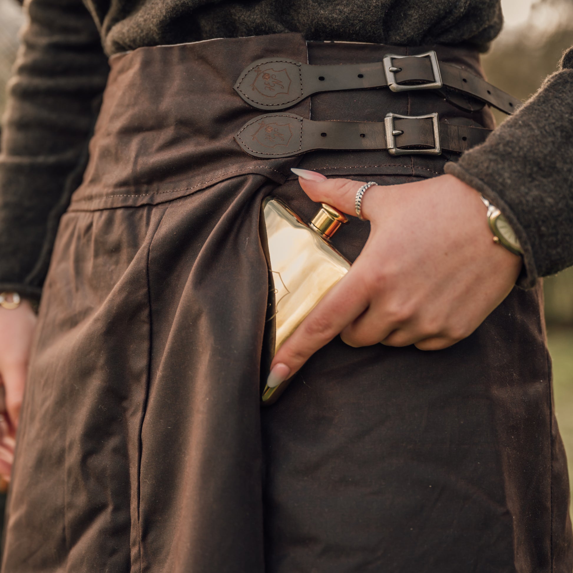 Showing a hip flask being put into the pocket of our British made waterproof habit.