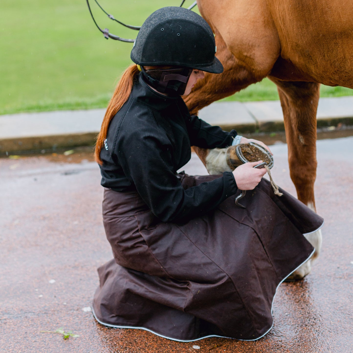 Brown waxed cotton riding habit being worn while picking out a horses foot.