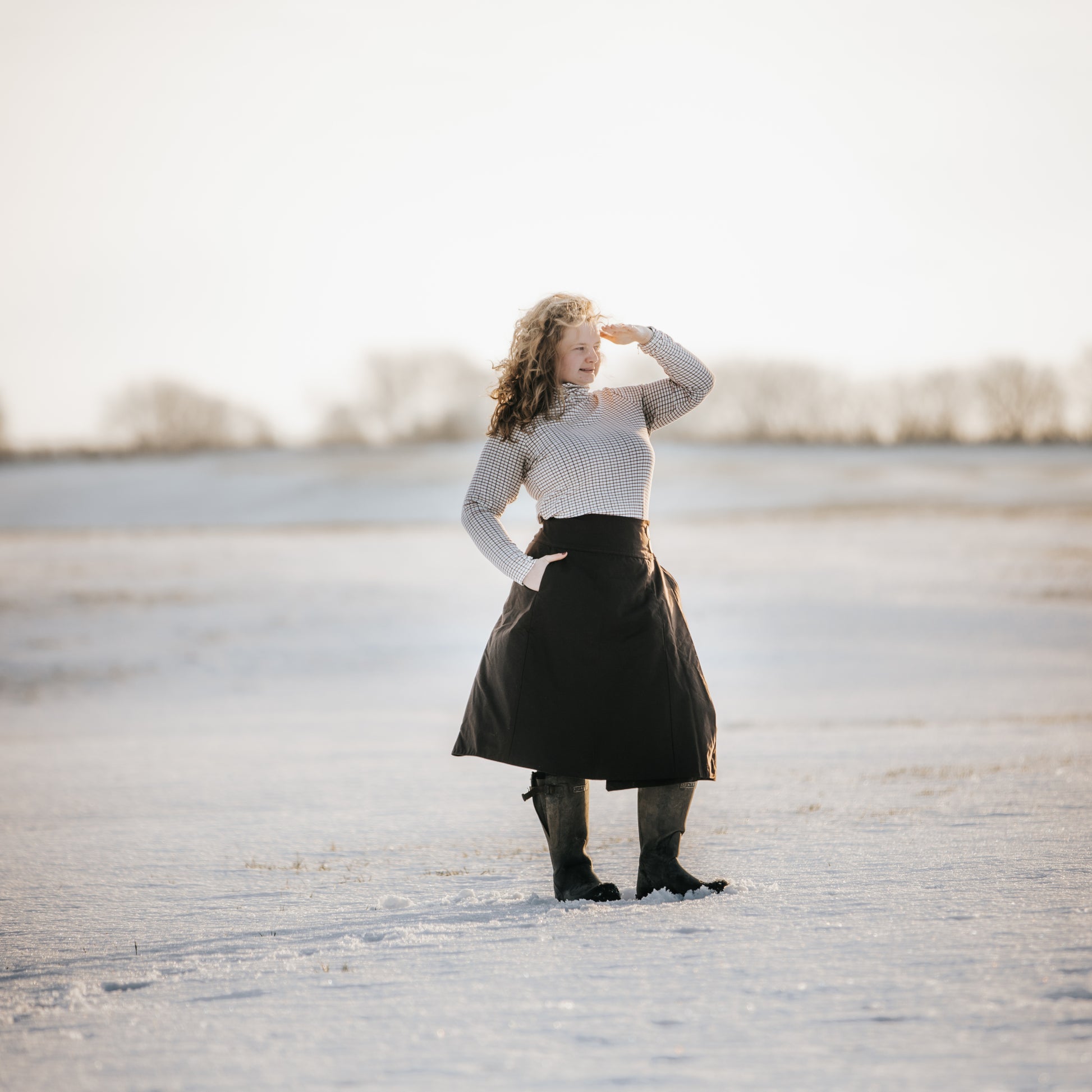 Lady stood looking into the distance surrounded by snow in the countryside, while wearing her handcrafted waxed habit.
