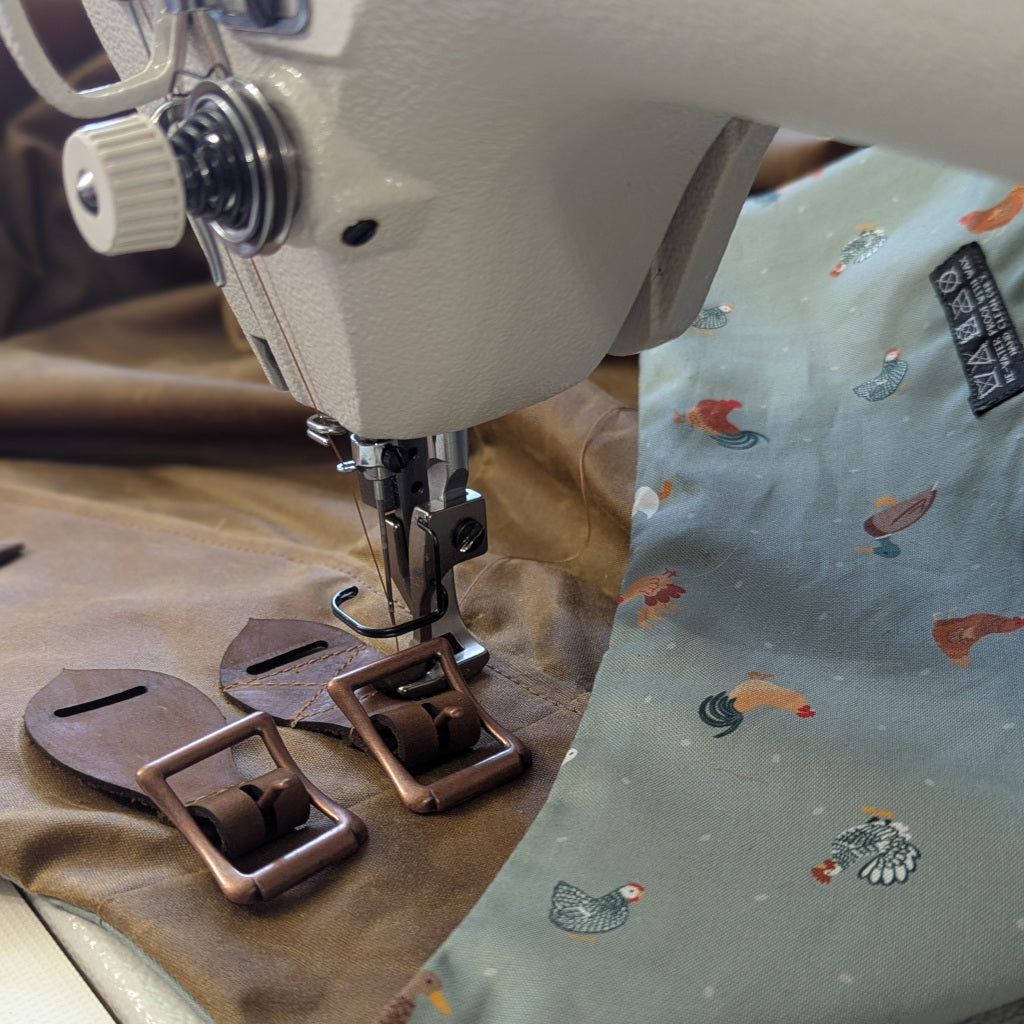 Close up of an industrial sewing machine sewing on the leather buckles to a waxed cotton habit in the Nouvelle habit studio.