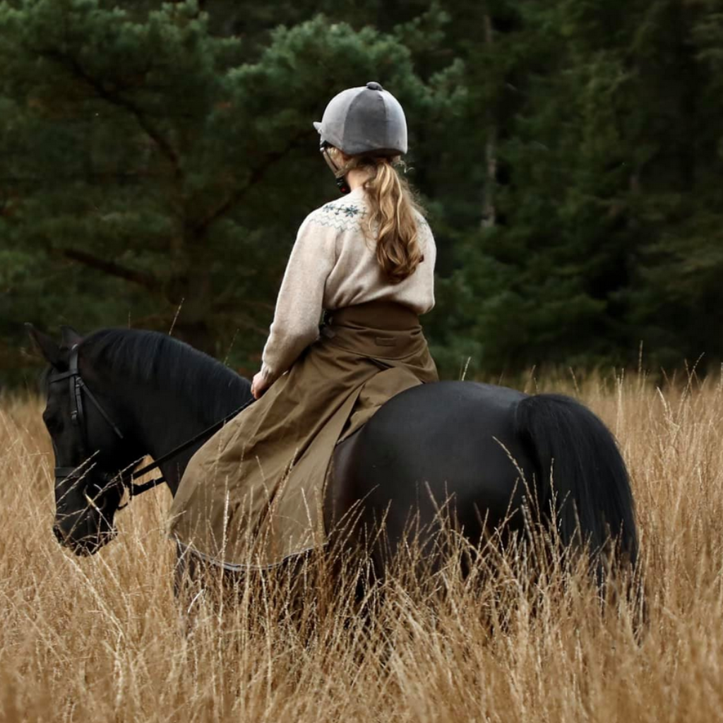Original Moorland riding skirt being worn  by a customer on her black horse in long grass.