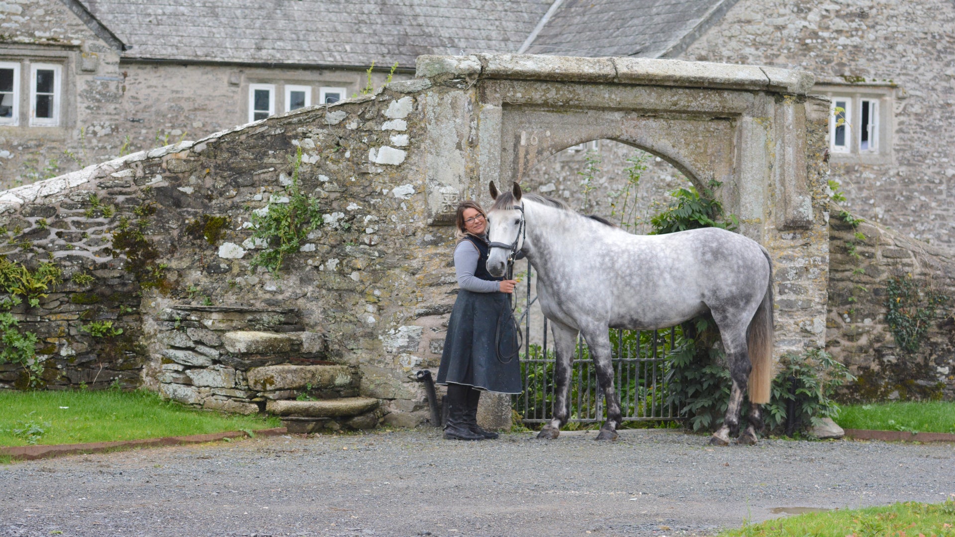 Hand crafted waterproof riding skirt, stood infront of a country house stone gateway
