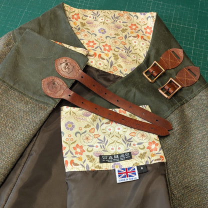 Brown leather buckle straps with floral lining on a Moss green tweed habit folded ontop of a cutting mat