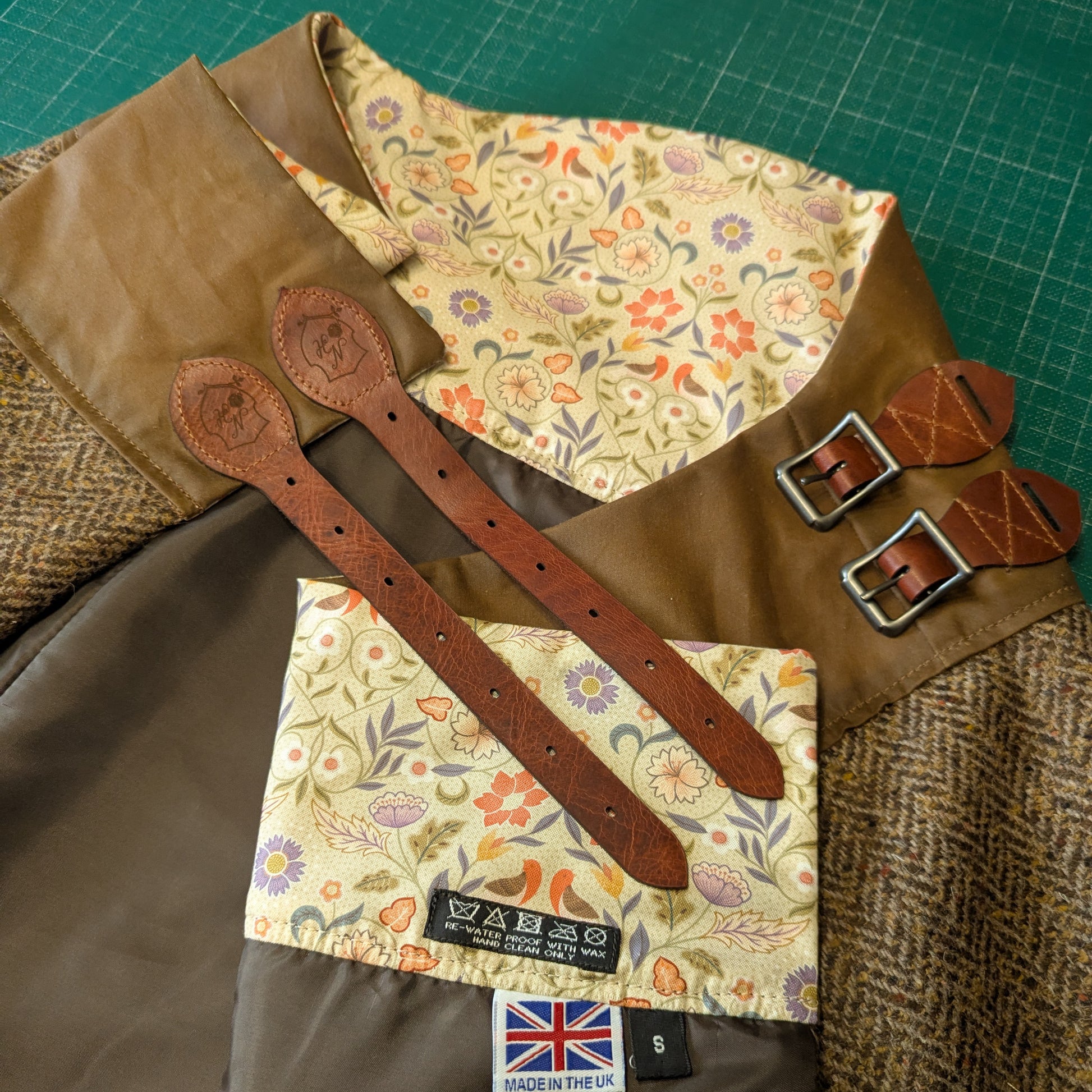 Herringbone tweed habit folded on a cutting mat showing the floral lining and leather buckle straps