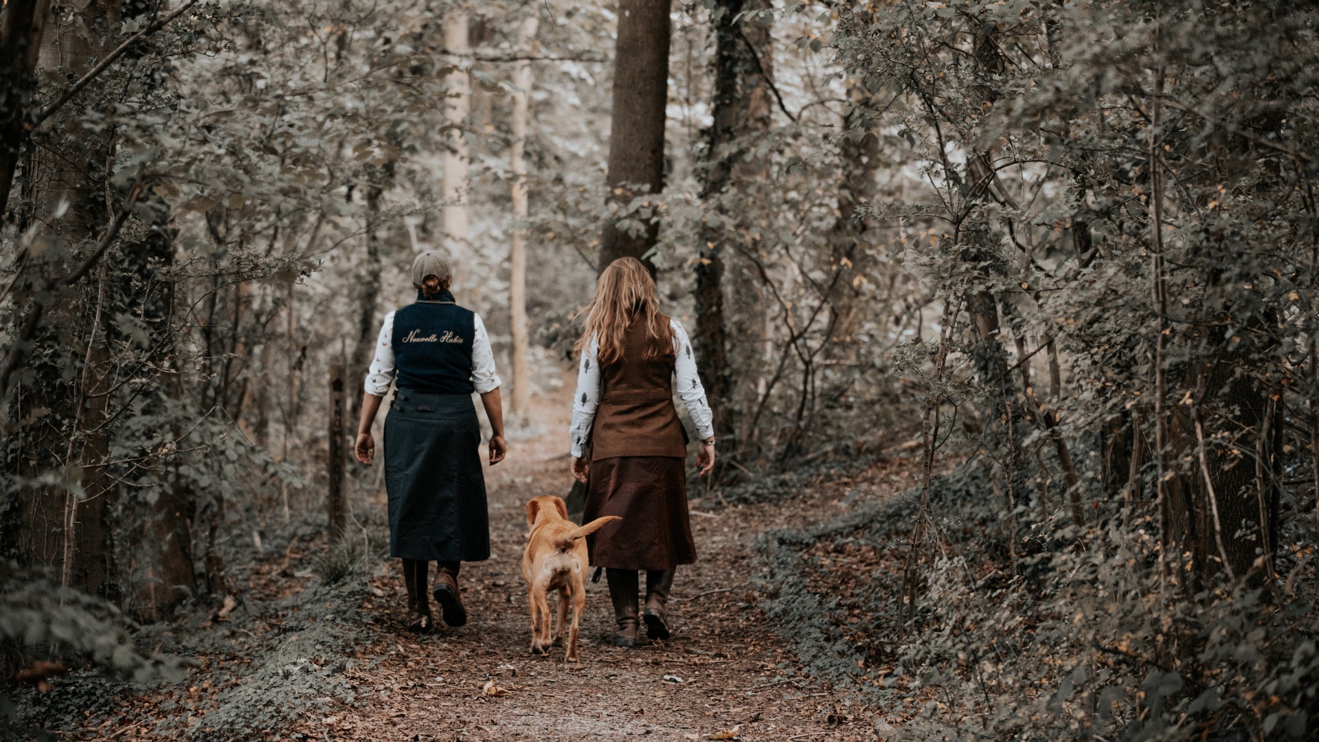 Two woman and there dog walking away in woodland wearing there hand crafted waterproof habits.