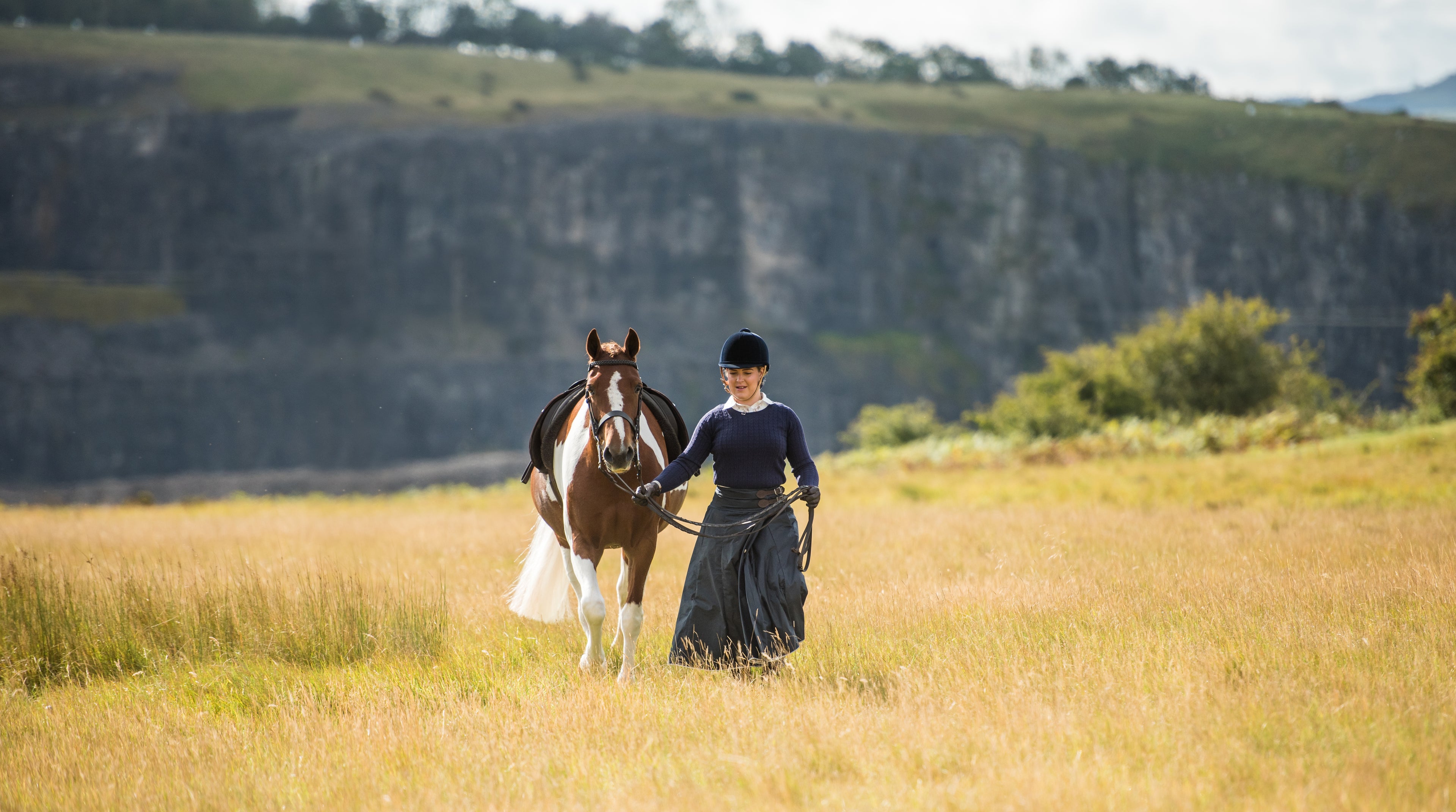 Woman leading her horse though a feild wearing her Moorland riding skirt.
