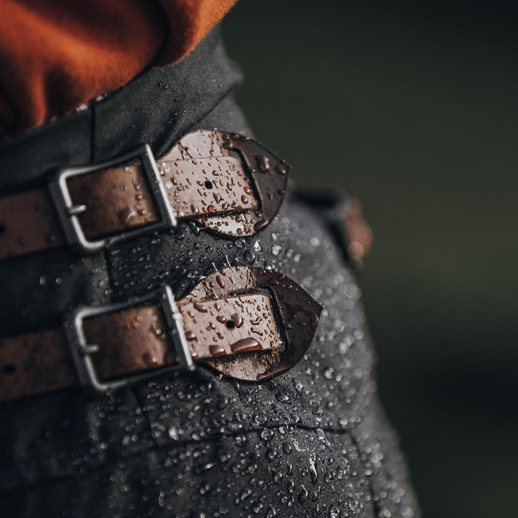 Close up of water droplets on the buckles at the top of a waterproof waxed cotton habit.