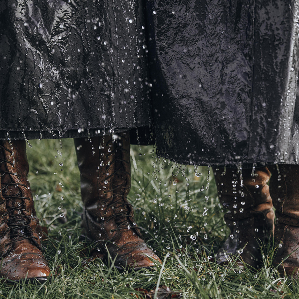 Water running of the bottom edge of two waxed cotton habits being worn over chunky leather boots, showing just how waterproof they are.