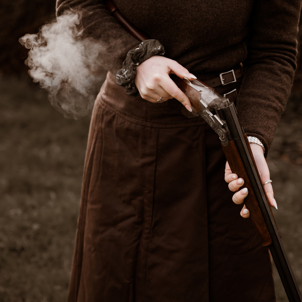 Smoking shot gun infront of a hand crafted shooting habit worn by a lady in a feild.